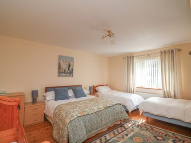 A bedroom with a double bed and two single beds near a window with curtains at Bolger House Ballintubbrid near Kilmuckridge County Wexford