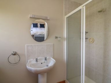 A bathroom with a pedestal sink and a shower enclosure with tiled walls at Bolger House in Ballintubbrid near Kilmuckridge County Wexford