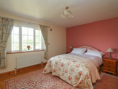 A bedroom with a double bed floral bedspread two bedside tables lamps and a window with curtains at Bolger House in Ballintubbrid near Kilmuckridge County Wexford