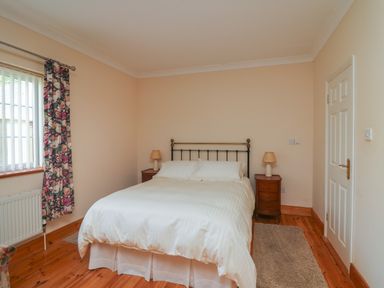 A bedroom with a double bed two bedside tables with lamps a window with floral curtains and a door at Bolger House Ballintubbrid near Kilmuckridge County Wexford