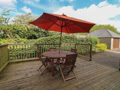 A wooden outdoor deck with a round table four chairs and a large umbrella at Bolger House in Ballintubbrid near Kilmuckridge County Wexford