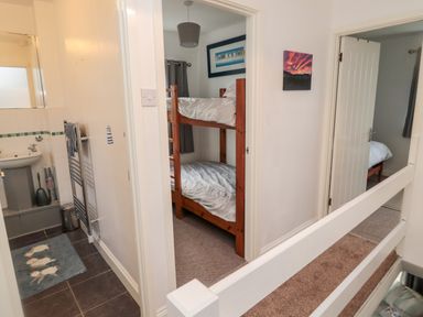 A hallway with doors leading to a bathroom with a sink and towel rack a bedroom with wooden bunk beds and another bedroom with a single bed at 22 Longstone Park Beadnell
