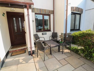An outdoor patio area with four wicker chairs and a table near a brown front door at Bumbles in Padstow