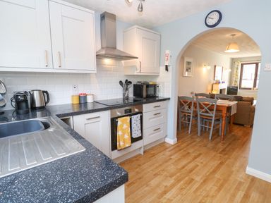 A kitchen with black countertops and white cabinets opening to a dining area with a wooden table and chairs at Bumbles in Padstow
