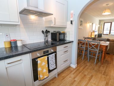 A kitchen with stove oven microwave and countertop utensils next to a dining table with chairs in a connected dining room at Bumbles in Padstow