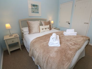 A bedroom with a double bed and beige pillows and blanket with two bedside tables and lamps at Bumbles in Padstow