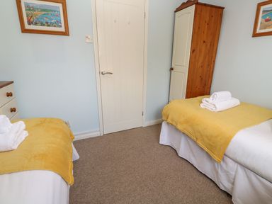 A bedroom with two single beds with yellow blankets and white towels a wooden wardrobe and framed paintings on the walls at Bumbles in Padstow