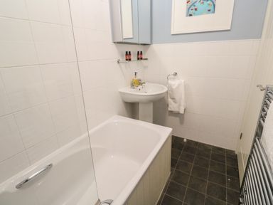 A bathroom with a bathtub sink mirror cabinet towel rail and framed picture at Bumbles in Padstow
