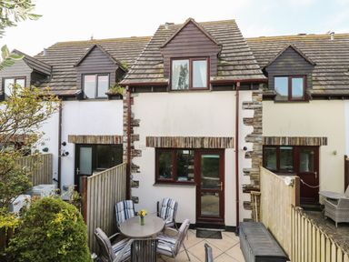 A small patio with table and chairs outside a two story house with stone and white walls at Bumbles in Padstow