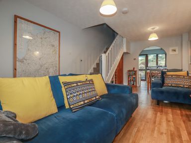 A living room with blue sofas and yellow cushions near a staircase and dining area at Bumbles in Padstow