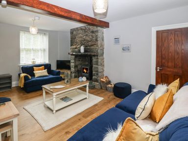 A living room with blue sofas a stone fireplace wooden coffee table and a wooden door at Belle View in Llaniestyn near Abersoch
