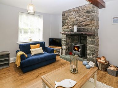 A living room with a stone fireplace a blue sofa a wooden coffee table and firewood at Belle View in Llaniestyn near Abersoch