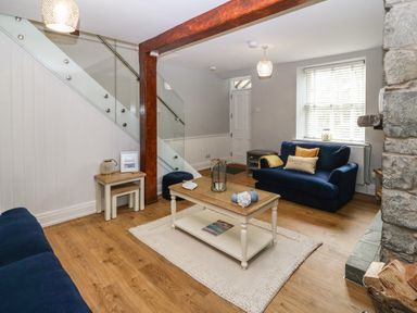 A living room with blue sofas a wooden coffee table and a staircase at Belle View in Llaniestyn near Abersoch