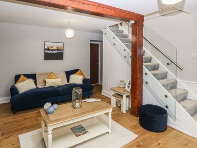 A living room with a blue sofa pillows a wooden coffee table a staircase with glass balustrade and a wooden pillar at Belle View in Llaniestyn near Abersoch