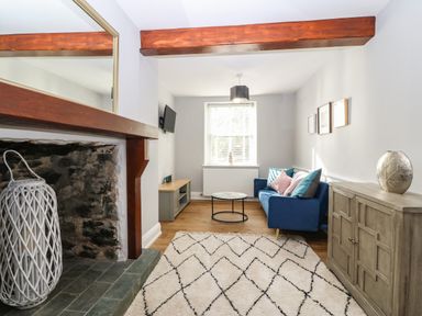 A living room with a stone fireplace and wooden mantle a blue sofa with cushions a round coffee table a wooden cabinet and a patterned rug at Belle View in Llaniestyn near Abersoch
