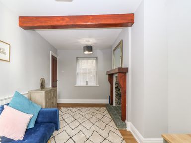 A living room with a blue sofa with cushions a wooden cabinet a window with white blinds a fireplace with a wooden mantel and a large mirror at Belle View in Llaniestyn near Abersoch