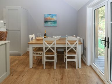 A dining area with a wooden table and white chairs near glass doors at Belle View in Llaniestyn near Abersoch
