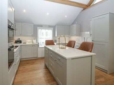 A kitchen with grey cabinets wooden floor an island with three brown chairs and a window at Belle View in Llaniestyn near Abersoch