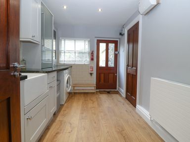 A utility room with white cabinets washing machine wooden floor and wooden doors at Belle View in Llaniestyn near Abersoch