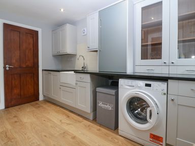 A laundry room with washing machine grey cabinets sink and wooden door at Belle View in Llaniestyn near Abersoch