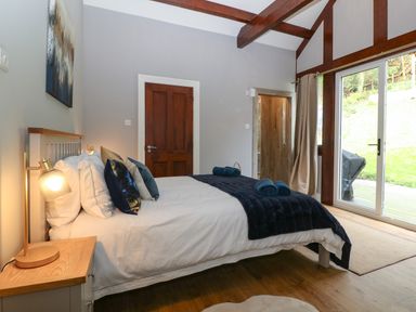 A bedroom with a bed a bedside table lamp wooden door and glass sliding door at Belle View in Llaniestyn near Abersoch