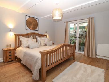 A bedroom with a wooden bed and beige bedding two bedside tables with lamps and a door with curtains at Belle View Llaniestyn near Abersoch