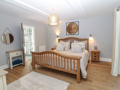 A bedroom with a wooden bed and nightstands a wall mirror and a door leading to a bathroom at Belle View in Llaniestyn near Abersoch