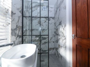 A bathroom with a white sink and a glass shower enclosure with marble tiles Bella View Llaniestyn near Abersoch