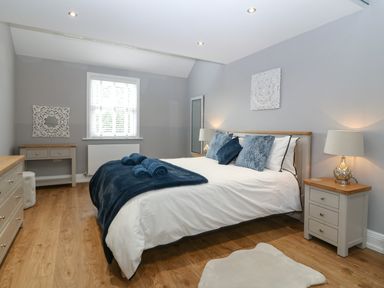 A bedroom with a double bed with pillows and towels bedside tables with lamps a dresser a side table a mirror and wooden flooring at Belle View in Llaniestyn near Abersoch
