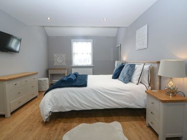 A bedroom with a bed bedside tables lamps a dresser a wall-mounted TV and a window at Belle View in Llaniestyn near Abersoch