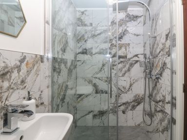 A bathroom with a sink and a glass-enclosed shower with marble-patterned tiles at Belle View in Llaniestyn near Abersoch