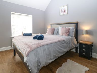 A bedroom with a double bed with pink and blue bedding bedside table with lamp and window at Belle View in Llaniestyn near Abersoch