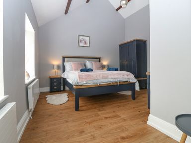 A bedroom with a double bed bedside tables lamps wardrobe and wooden floor at Belle View Llaniestyn near Abersoch