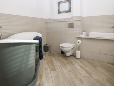 A bathroom with a bathtub, toilet, sink, mirror, and wooden floor at Belle View in Llaniestyn near Abersoch