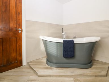 A freestanding bathtub with a towel hanging on it in a bathroom with tiled walls and wooden door at Belle View in Llaniestyn near Abersoch