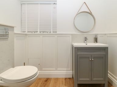A bathroom with a toilet, sink with cabinet, mirror, and window blinds at Belle View in Llaniestyn near Abersoch