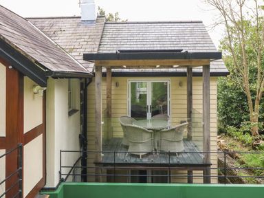 An outdoor balcony with a glass table and woven chairs attached to a house with a glass railing at Belle View in Llaniestyn near Abersoch