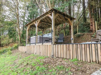 A wooden gazebo with a hot tub and chairs on a raised platform in a wooded area at Belle View in Llaniestyn near Abersoch