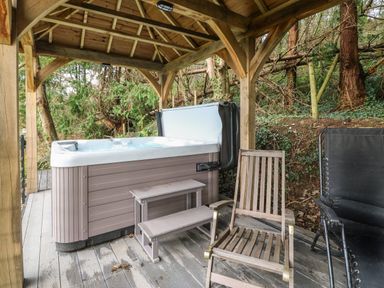 An outdoor hot tub under a wooden gazebo with stairs and two chairs surrounded by trees at Belle View in Llaniestyn near Abersoch