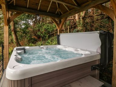 An outdoor hot tub with bubbling water under a wooden pergola surrounded by trees at Belle View in Llaniestyn near Abersoch