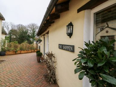 The exterior wall of a building with a sign reading The Shippen a paved walkway and plants in pots near the building at The Shippen in Gooseham near Kilkhampton