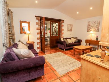 A living room with two purple sofas and a wooden coffee table with open wooden doors at The Shippen in Gooseham near Kilkhampton