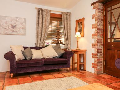 A living room with a purple sofa and cushions next to a wooden side table with a lamp at The Shippen in Gooseham near Kilkhampton