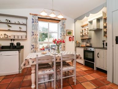 A kitchen with a dining table and chairs a window with curtains kitchen appliances and shelves at The Shippen in Gooseham near Kilkhampton