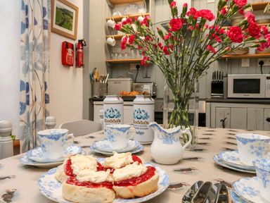 A kitchen table set with blue and white china cups and saucers scones with cream and jam a vase with red flowers and cans of Rodda's clotted cream in a kitchen at The Shippen Gooseham near Kilkhampton
