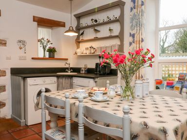 A kitchen with a table set with cups and flowers on it and appliances along the wall at The Shippen in Gooseham near Kilkhampton