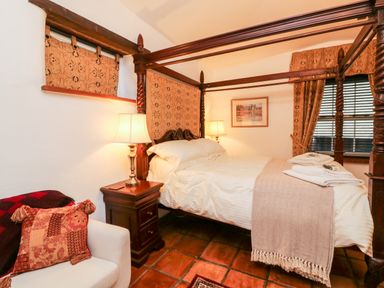 A bedroom with a four-poster bed bedside tables with lamps a small sofa with cushions and a framed picture on the wall at The Shippen in Gooseham near Kilkhampton