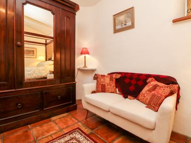 A small sitting area with a white sofa with patterned cushions and a red lamp on a wall shelf at The Shippen in Gooseham near Kilkhampton