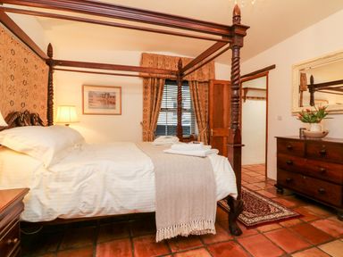 A bedroom with a wooden four-poster bed a wooden dresser and a window with curtains at The Shippen in Gooseham near Kilkhampton