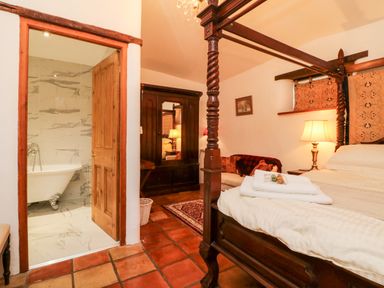 A bedroom with a four poster bed a wardrobe a sofa and an open door to a bathroom with a clawfoot bathtub at The Shippen in Gooseham near Kilkhampton